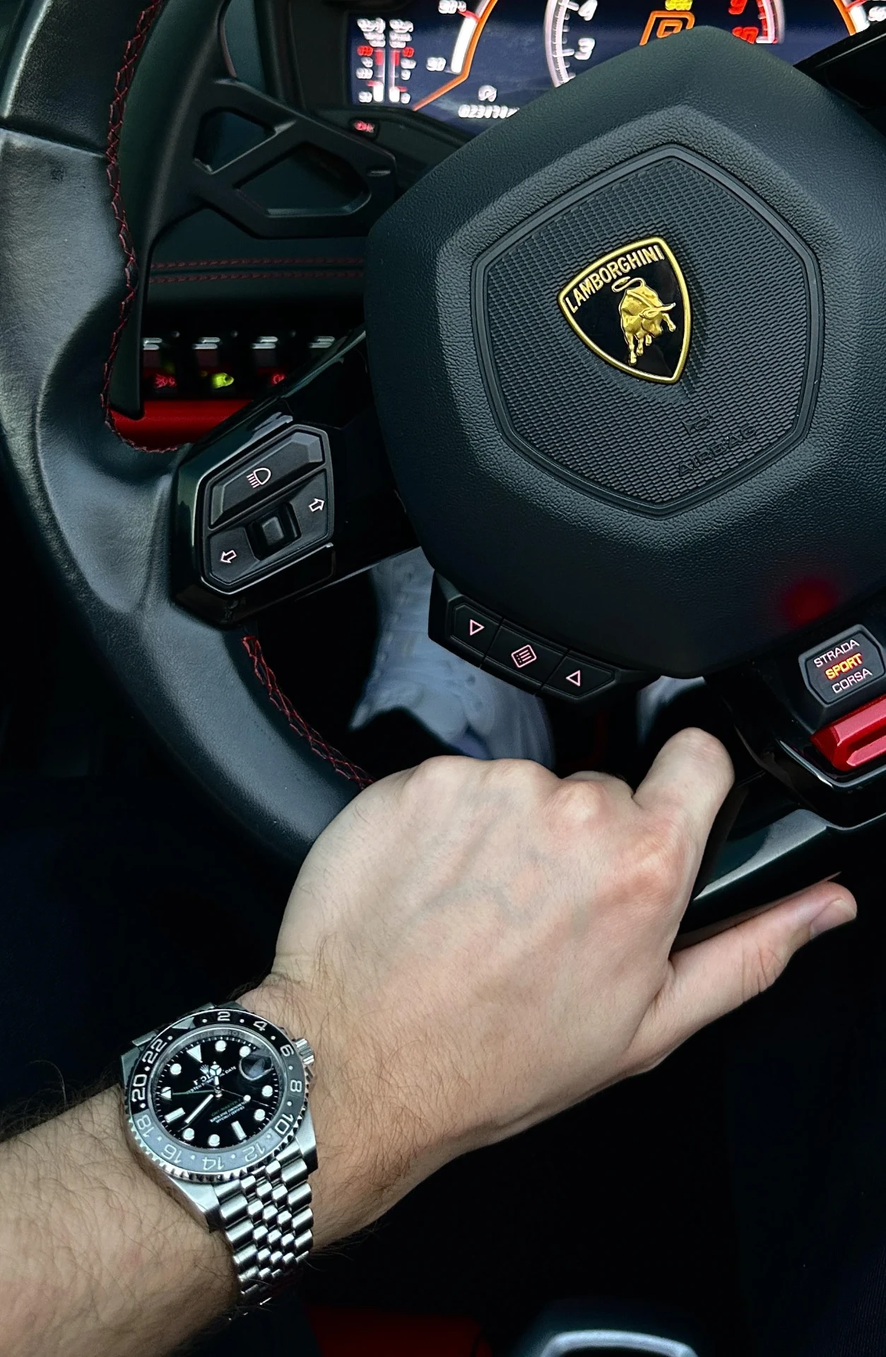 Stainless steel GMT watch on the wrist behind a Lamborghini steering wheel