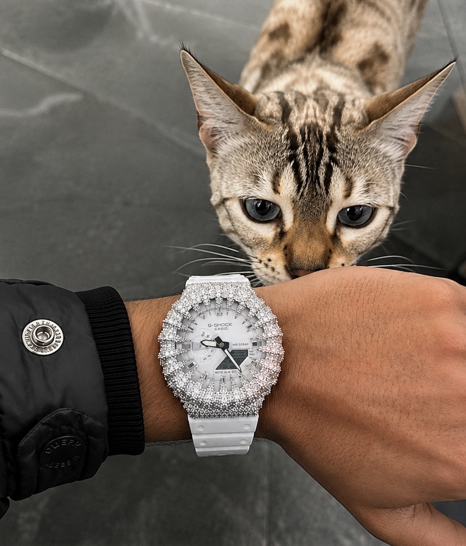 White iced-out G-Shock on a wrist with a cat in the background